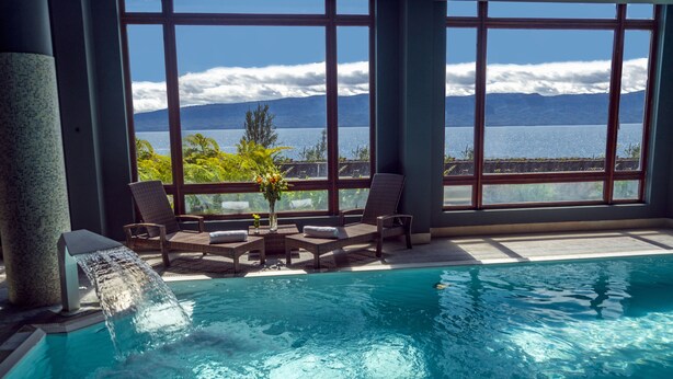 Un área de piscina con una cascada, sillas de descanso y vistas a un lago y montañas.