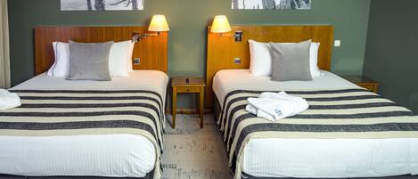 Two double beds with striped bedding, wooden headboards, bedside lamps, and a white carpet.