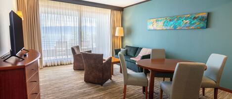 Habitación de hotel con un escritorio de madera, dos sillones, un sofá, un televisor y un cuadro en la pared.