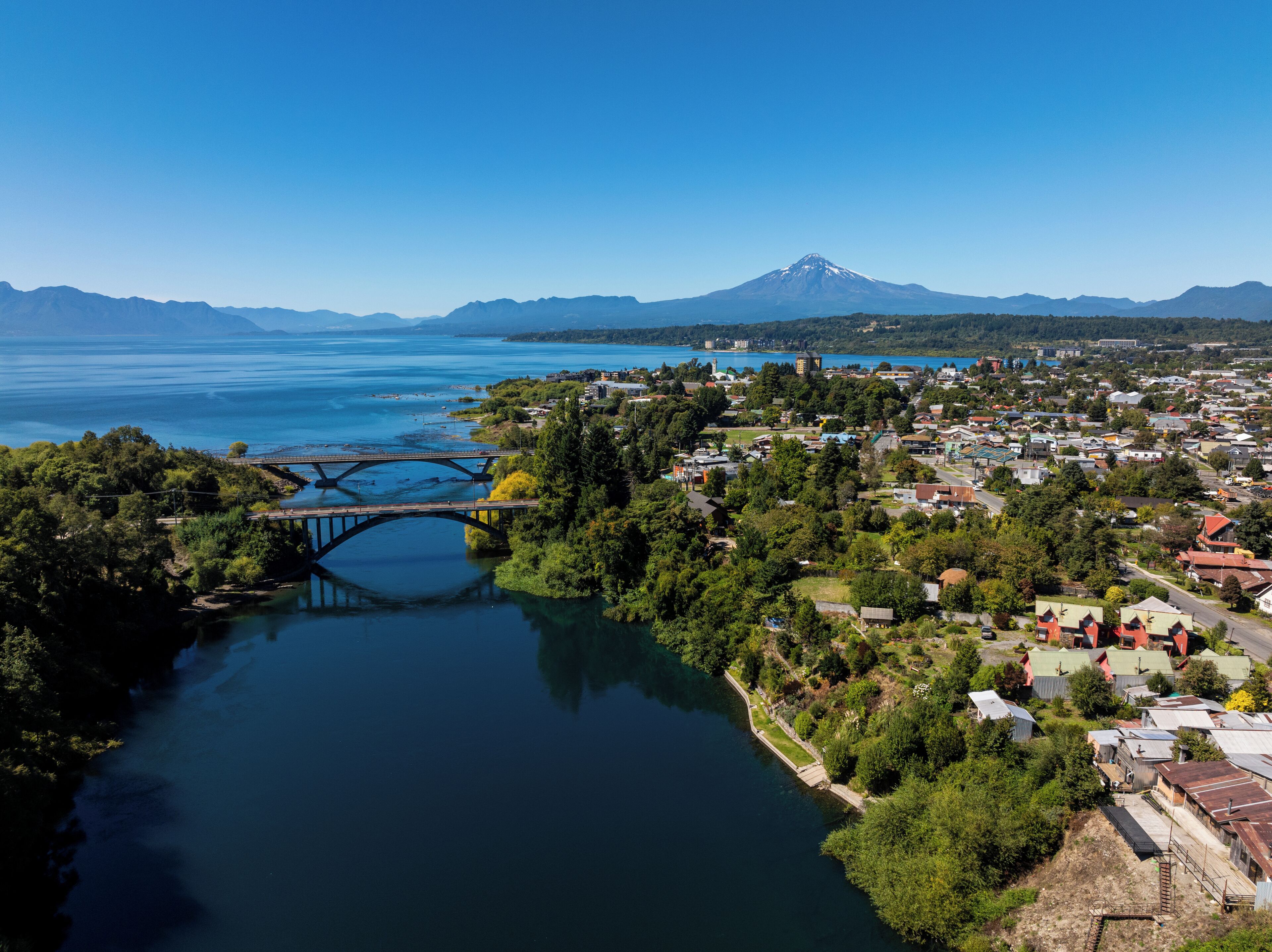 A town with a bridge over a river, surrounded by mountains and a lake.