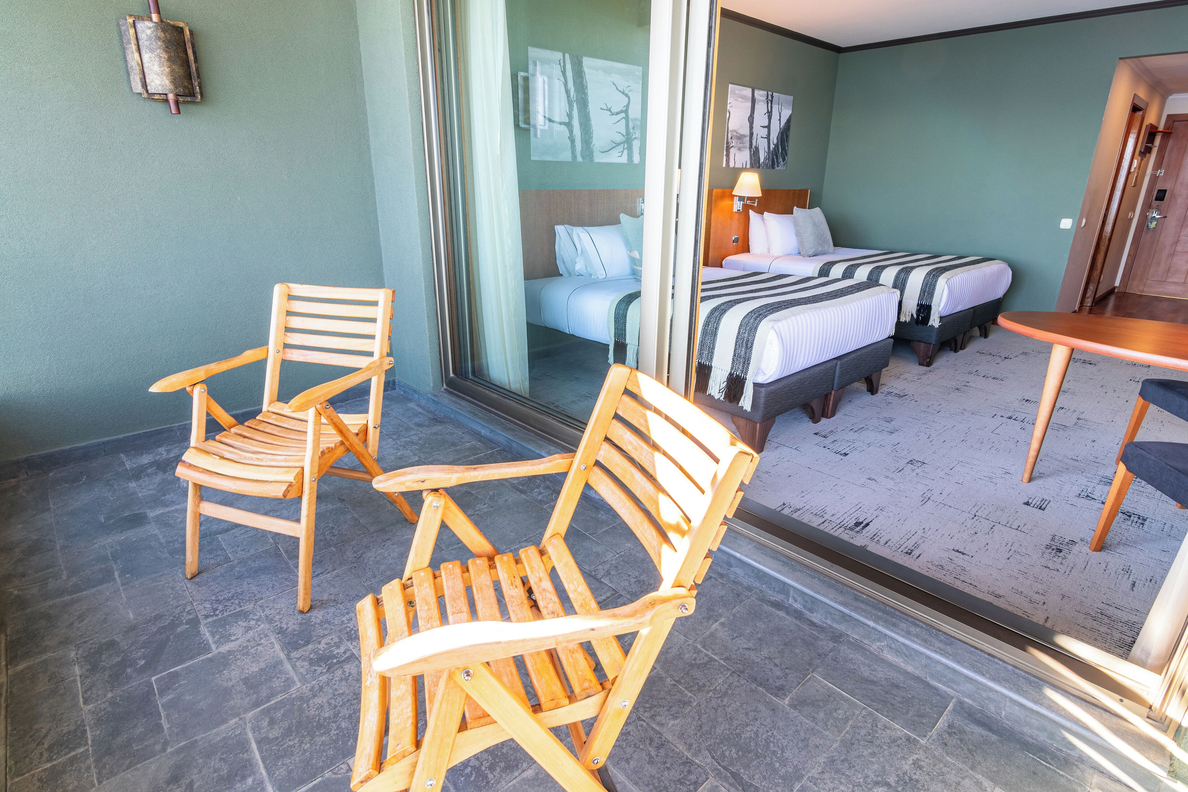 A hotel room with two wooden chairs, a bed with a striped blanket, and a small table.