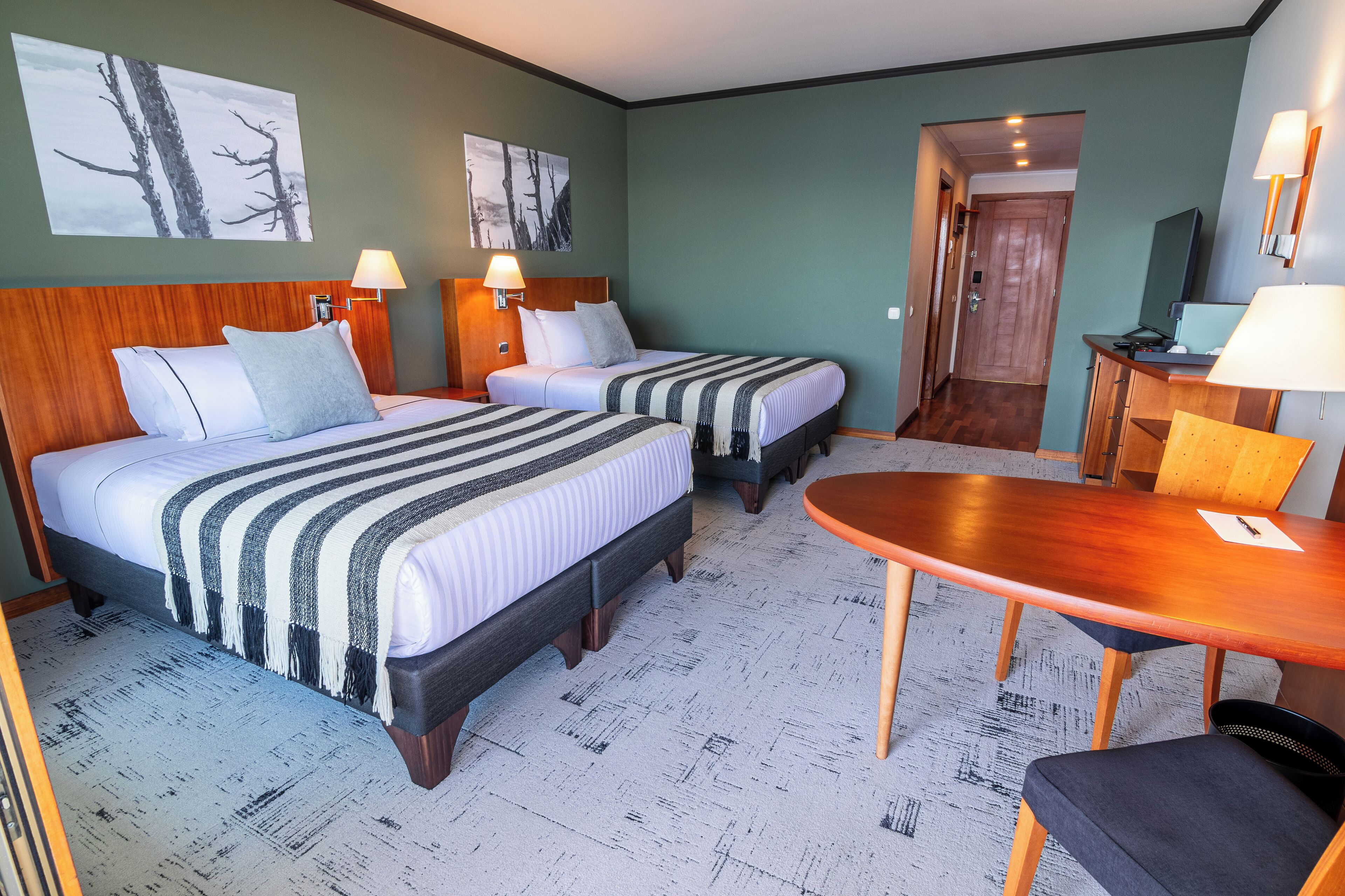 A hotel room with two beds, a wooden table, and a desk with a chair.