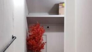 Een trap met een leuning aan de linkerkant, leidend naar een kamer met een witte deur en een rode decoratie.