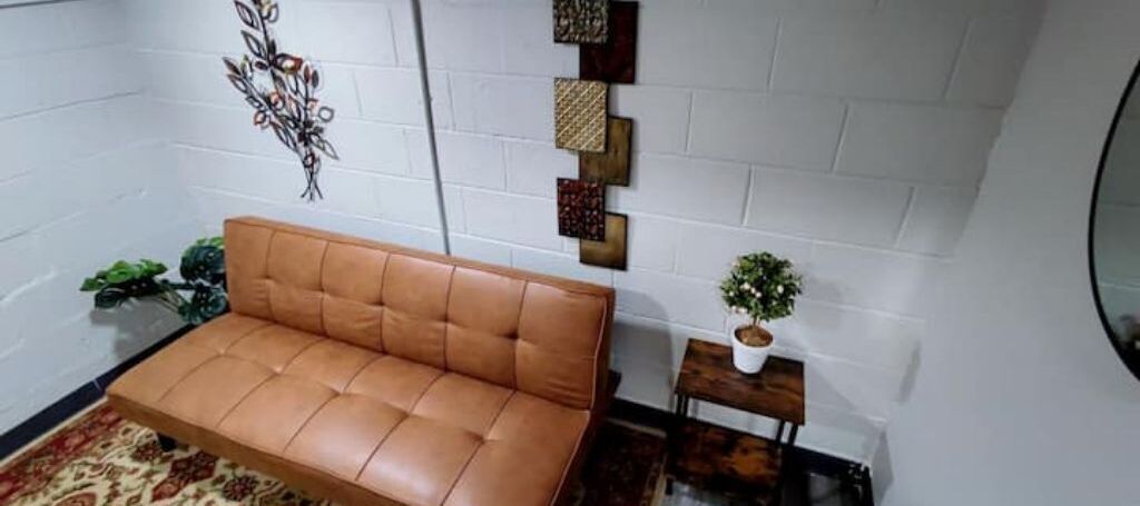 Une pièce avec un canapé en cuir marron, une petite table d’appoint en bois sur laquelle est posée une plante, et des œuvres d’art décoratives accrochées au mur.
