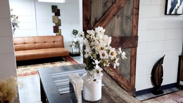 Een woonkamer met een bruine leren bank, een witte vaas met witte bloemen, een houten kast en een televisie op een houten dressoir.