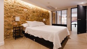 A bedroom with a stone wall, a bed with white linens, a nightstand with a lamp, and a view through a glass door. - Lefevre 1B (Panama City)