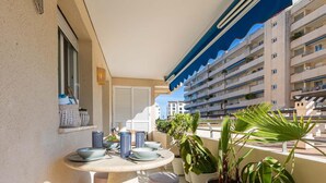 A balcony with a table set for dining, potted plants, and a view of a multi-story building. - Puerto Banús Cozy and Luxe Home (Marbella)