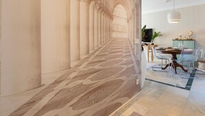 A corridor with columns and a patterned floor, leading to a dining area with a table, chairs, and a hanging light fixture. - Puerto Banús Cozy and Luxe Home (Marbella)