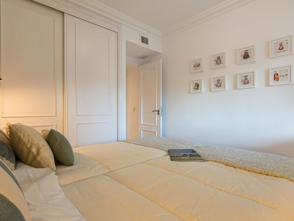 Un dormitorio con cama, almohadas, mesita de noche y un cuadro con marcos en la pared.