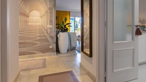 A hallway with a patterned floor, a large white vase with plants, and a mirror on the wall. - Puerto Banús Cozy and Luxe Home (Marbella)