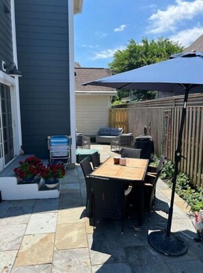 Relax under the shade of a large umbrella, surrounded by lush potted plants and a comfortable seating area.