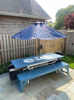 Enjoy a patio with a shaded table and bench set, surrounded by a grassy lawn and wooden fence.