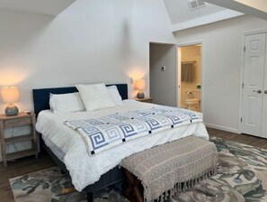 Experience a spacious and airy room with a high ceiling, featuring a central bed, bedside tables, and a cozy throw blanket.