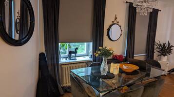 Uma sala de jantar com mesa de vidro, cadeiras modernas, um lustre e vista para o verde lá fora.