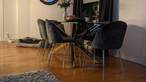 Zona pranzo con tavolo rotondo, sedie nere, un lampadario, uno specchio e un'ampia finestra con tende.