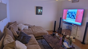 Un soggiorno con una grande TV a schermo piatto, un divano, un tavolino da caffè e un piccolo tavolino laterale con tastiera e mouse.