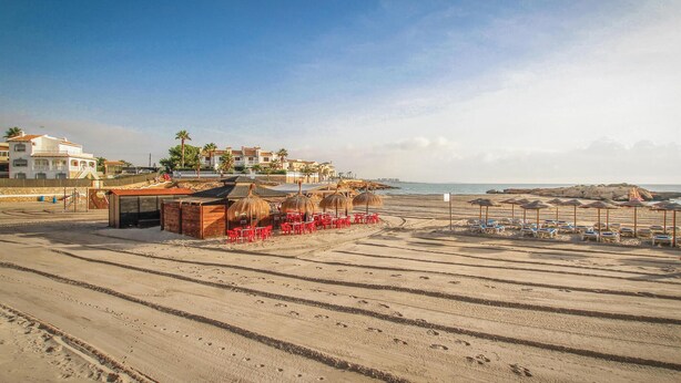 Een strand met een rieten hut, rode plastic stoelen en parasols.