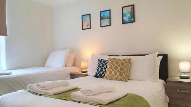 Une chambre d’hôtel avec deux lits, un plaid vert et une table de chevet avec une lampe.