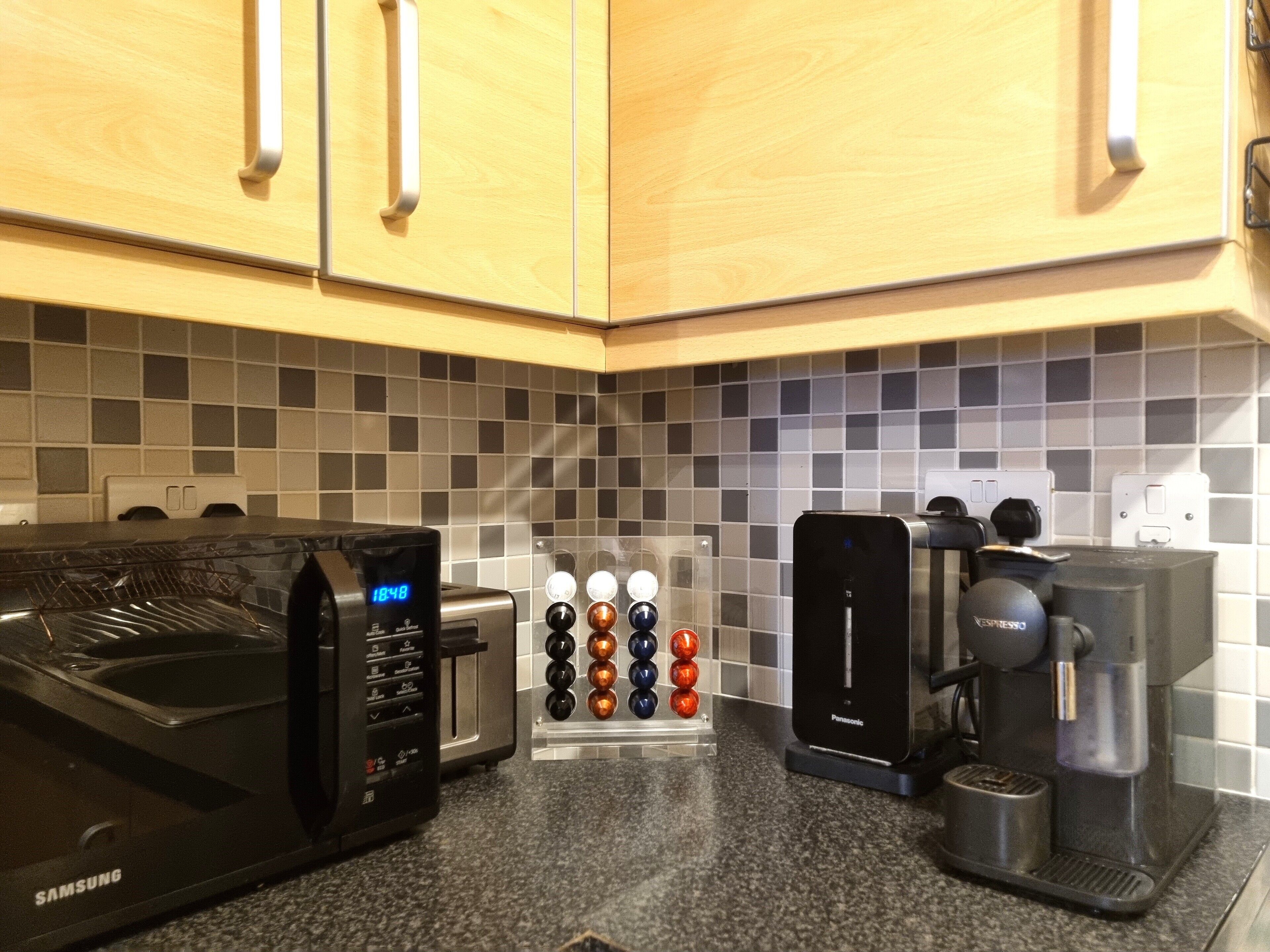 A kitchen with a microwave, coffee maker, and a coffee pod dispenser.