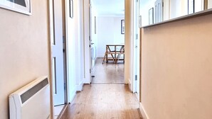 Un couloir doté d’un plancher en bois, de murs blancs et de tableaux encadrés sur le côté gauche.