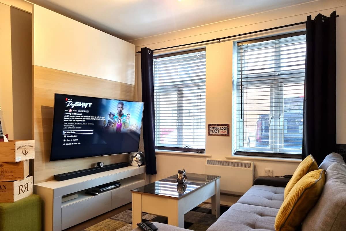 A modern living room with a flat-screen TV, a sofa, a coffee table, and a window with blinds.