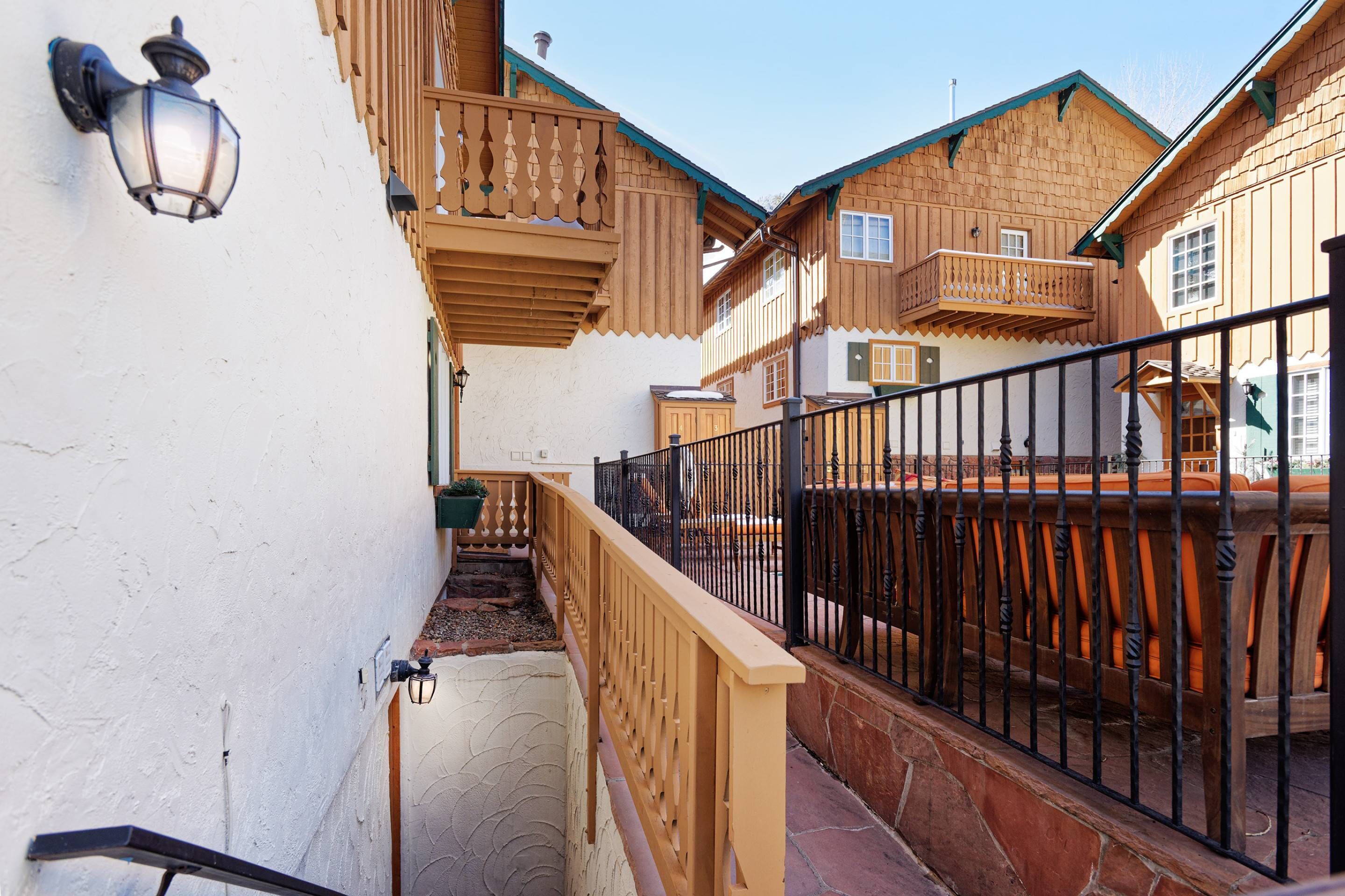 A narrow alleyway with wooden houses, a black metal fence, and a small staircase.