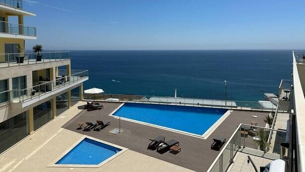 A rooftop pool with lounge chairs and a view of the ocean.