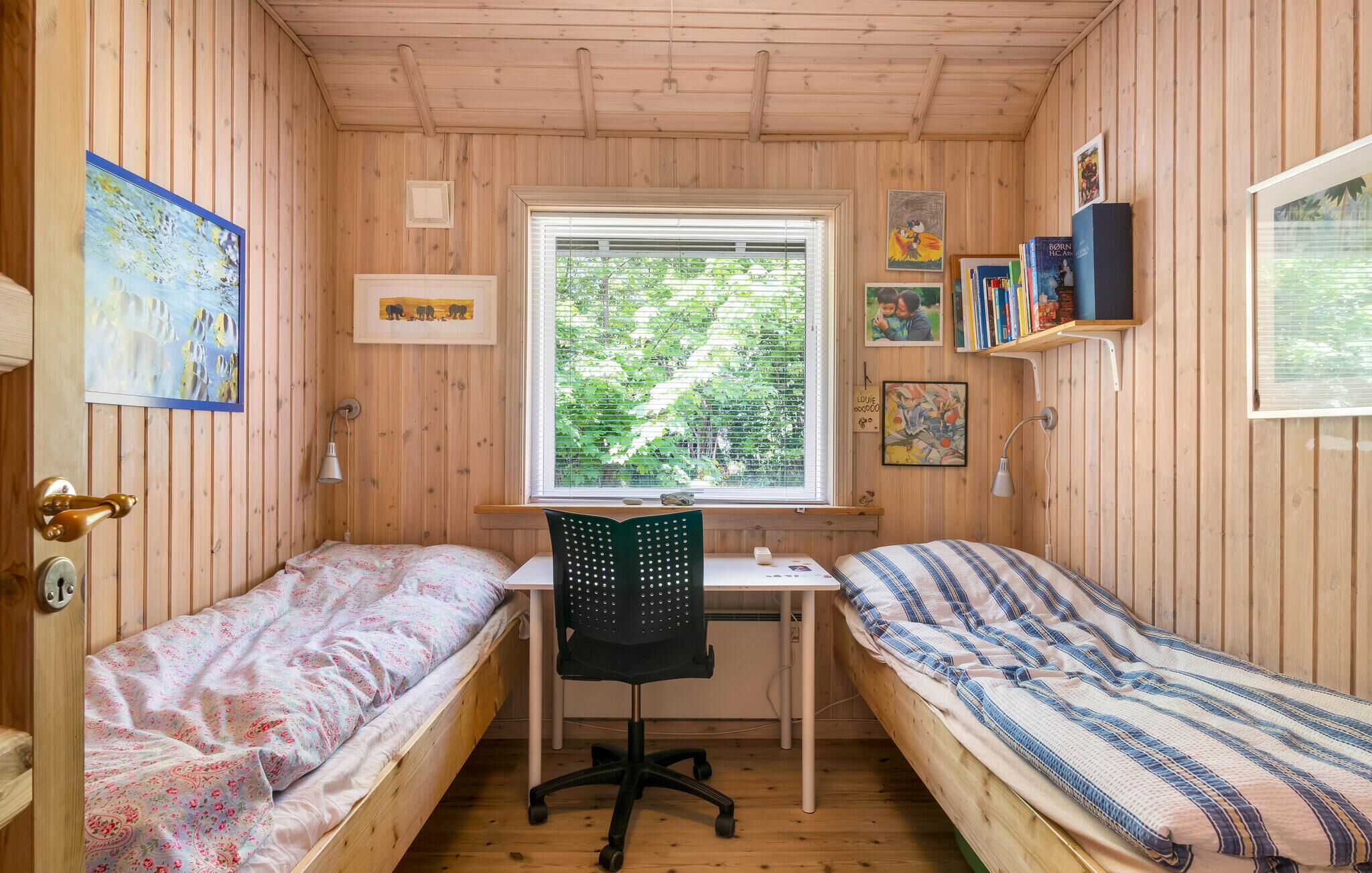 A cozy cabin with two wooden bunk beds, a desk with a chair, and a window with a view of greenery.