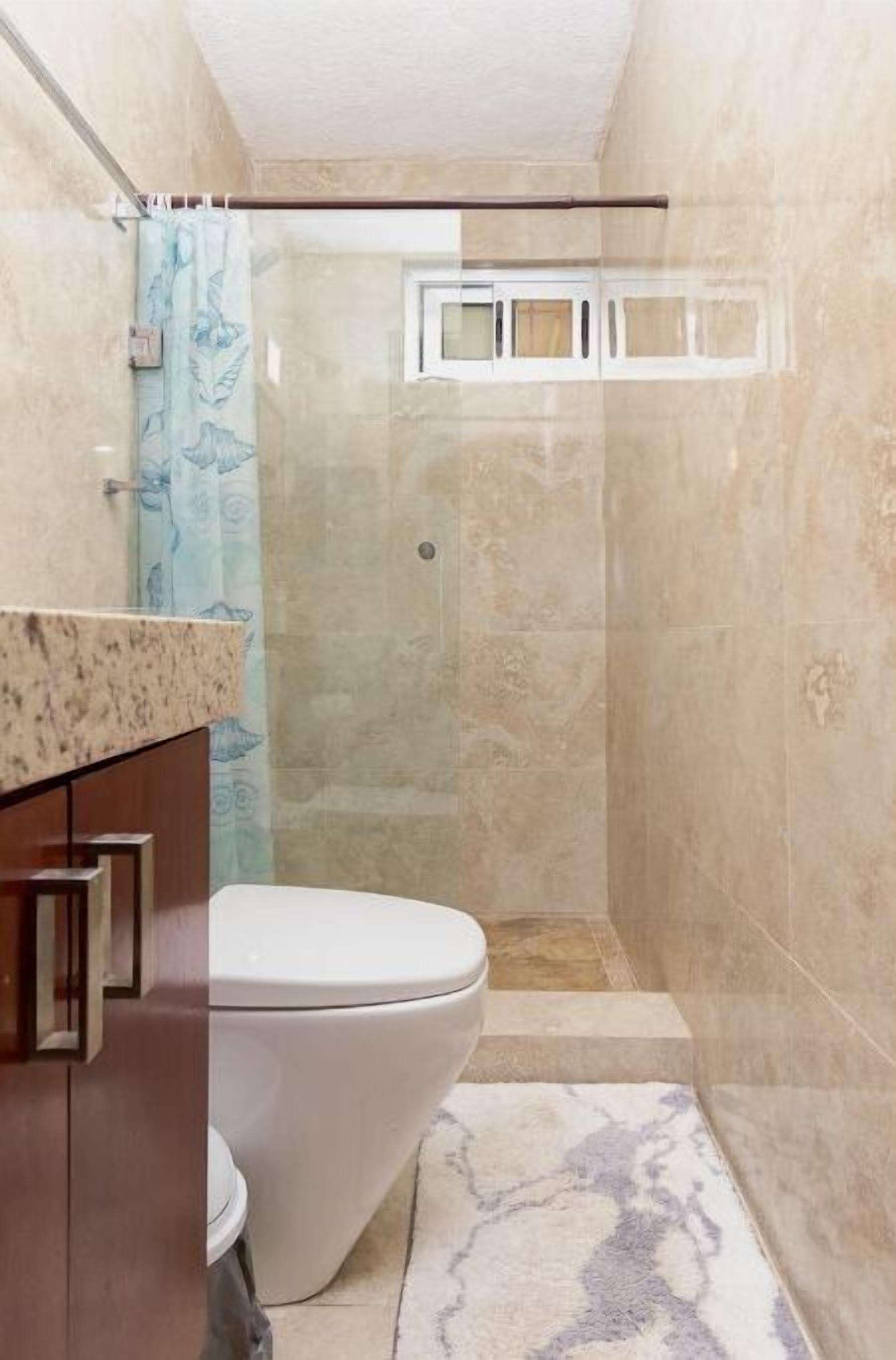 A bathroom with a toilet, shower, and a marble-tiled floor.