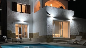 Une maison moderne à deux étages, dotée d’une piscine, de grandes fenêtres et d’un intérieur bien éclairé.