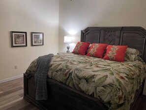 Een slaapkamer met een groot bed, een nachtkastje, twee ingekaderde foto’s en een lamp.