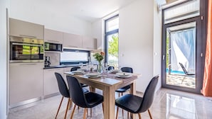 A modern kitchen with a dining area, large windows, and a view of the outdoors.
