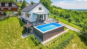 A house with a swimming pool, a covered patio, and a view of the surrounding greenery.