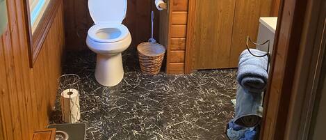 A small, wooden-paneled bathroom with a toilet, a towel rack, and a trash bin.