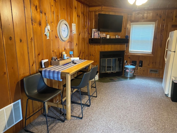 A cozy cabin interior with a wooden dining table, chairs, a fireplace, and a television mounted above it. - 2 bedroom Cabin, perfect beach getaway (Greenbush)