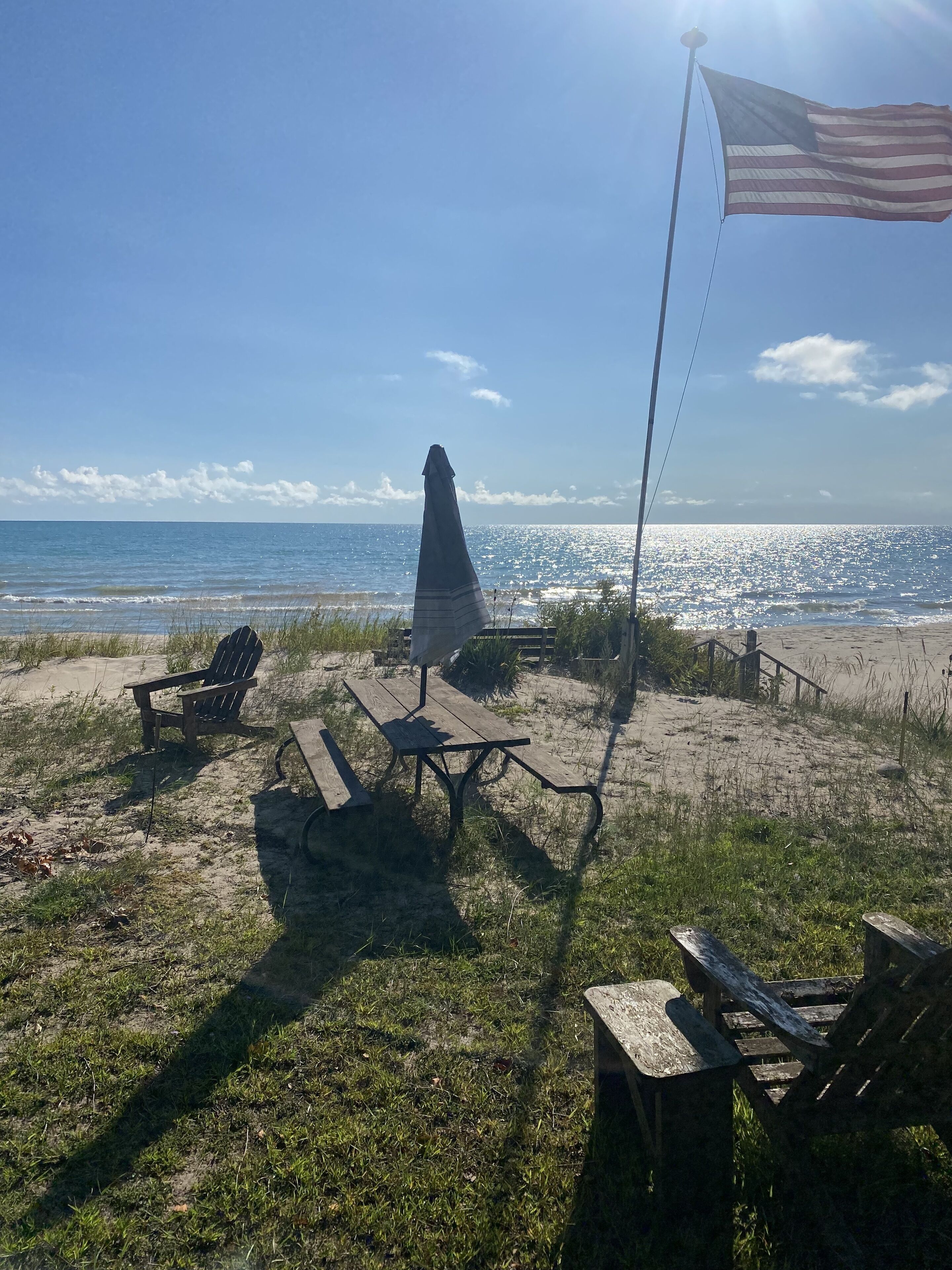 Een strand met een houten picknicktafel en stoelen, een vlaggenmast met de Amerikaanse vlag, en een hoog monument op de achtergrond.