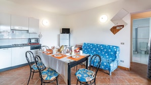 A compact kitchen with a gas stove, a refrigerator, and a microwave. There is a dining table with chairs and a blue sofa. - Beach front apartment in Isola Rossa (Isola Rossa)