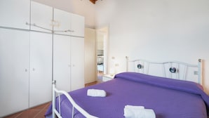 A bedroom with a bed, white wardrobe, and a bathroom visible in the background. - Beach front apartment in Isola Rossa (Isola Rossa)