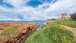 A coastal landscape with a historic stone tower, rocky terrain, and a narrow stream. - Beach front apartment in Isola Rossa (Isola Rossa)