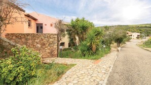A stone pathway leading to a pink building with a stone wall, surrounded by greenery and a rural landscape. - Beach front apartment in Isola Rossa (Isola Rossa)