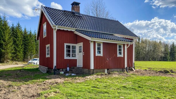 Ein rotes Holzhaus mit Ziegeldach, Schornstein und einer kleinen Veranda.