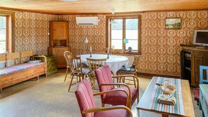 Ein gemütliches Zimmer mit Holzbalkendecke, strukturierter Tapete, einem runden Tisch mit Stühlen, einer Bank und einem Fernseher.