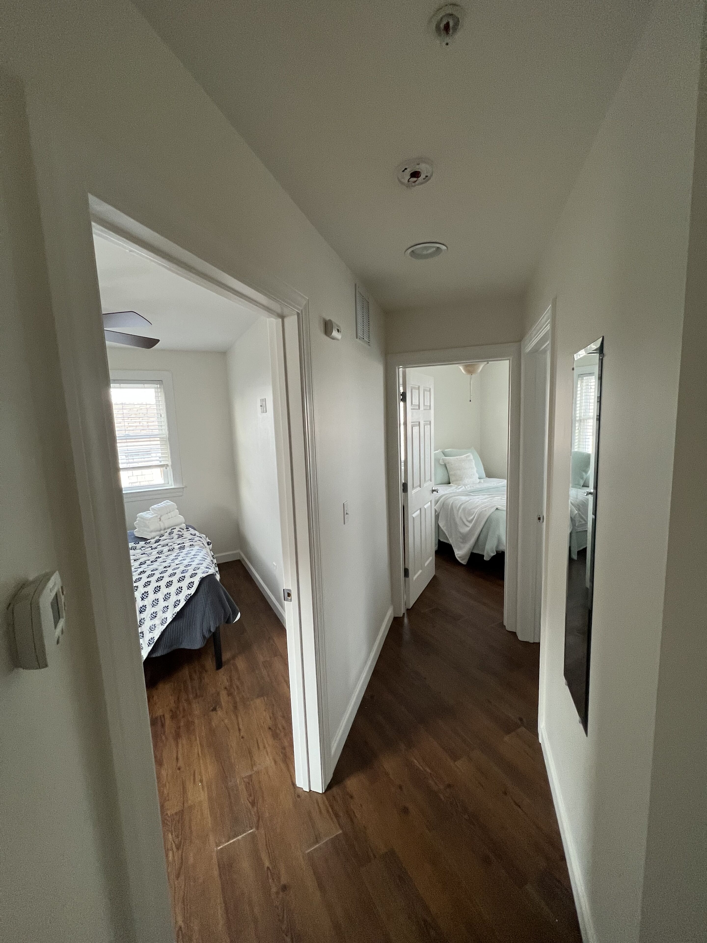 A hallway leading to a bedroom with a bed, a door, and a window.