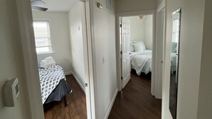 A hallway leading to a bedroom with a bed, a door, and a window.