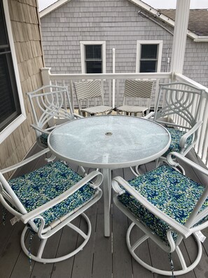 Una mesa redonda con sillas de metal blanco y cojines azules estampados sobre una terraza de madera.