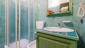 Een badkamer met een douchecabine van glas, een wastafel met een groen aanrechtblad en een klein plankje met een mand en bloemen.