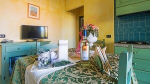 Een kamer met een bed, een televisie, een eettafel met een fles, een vaas met bloemen en groene kasten.
