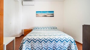 A bedroom with a bed, a nightstand, a wall-mounted air conditioner, and a beach landscape painting. - Cozy apartment in Ubrique with WiFi (Ubrique)