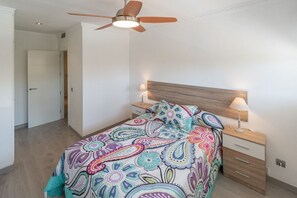 A bedroom with a bed, a ceiling fan, bedside lamps, and a wooden headboard. - Cortadura Beach Apartment (Cádiz)