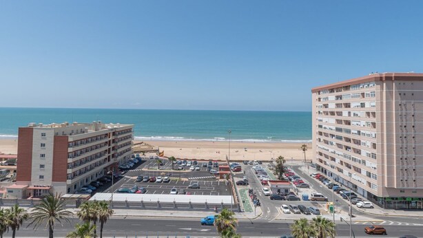 Een hotel aan de kust met meerdere verdiepingen, een parkeerplaats en uitzicht op het strand en de oceaan.